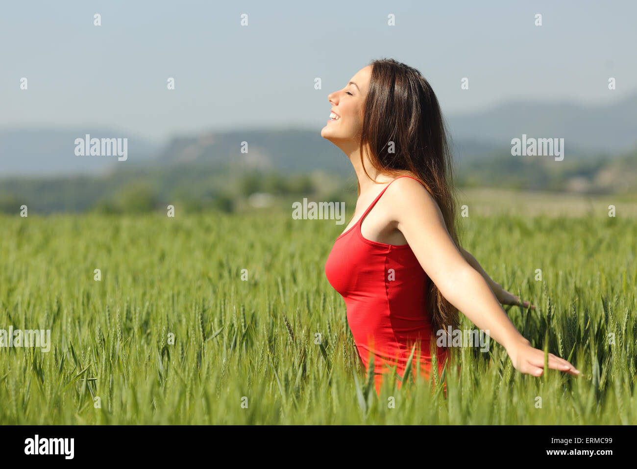 Profil d'une femme de respirer l'air frais dans un pré et toucher le blé vert portant une chemise rouge Banque D'Images
