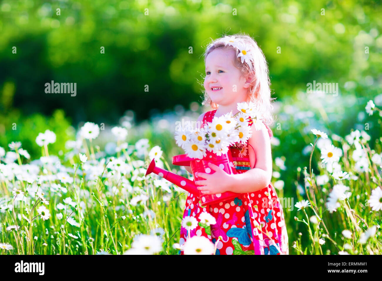 Jardinage pour enfants. Petite fille avec de l'eau peut dans un champ de fleurs Daisy. Enfants jouant dans le jardin avec des fleurs. Banque D'Images