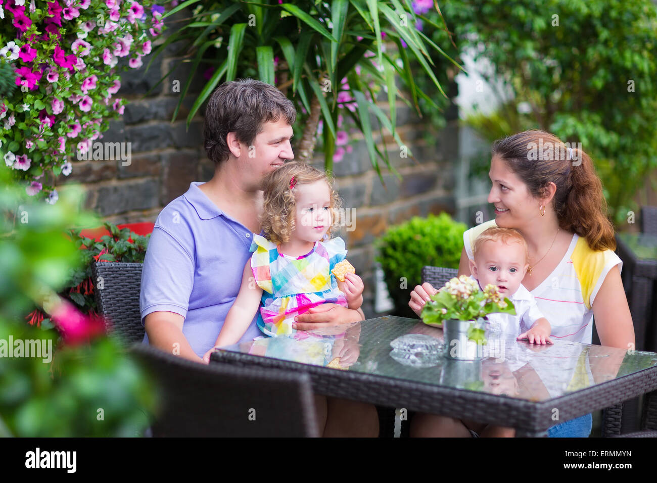 Heureux jeune famille, parents de deux enfants de manger le déjeuner dans un magnifique café en plein air avec des fleurs dans une ville Banque D'Images