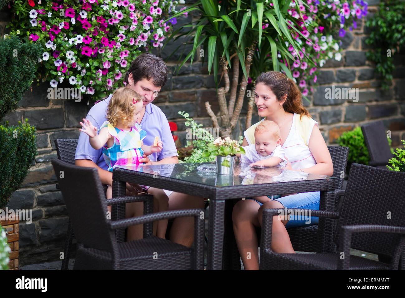 Heureux jeune famille, parents de deux enfants de manger le déjeuner dans un magnifique café en plein air avec des fleurs dans une ville Banque D'Images