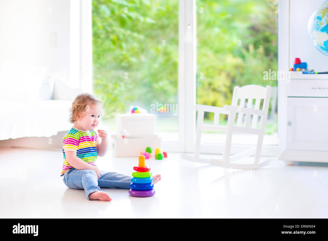 Adorable petit bébé fille dans une chemise colorée à jouer avec un jouet pyramide et blocs de construction assis sur le plancher Banque D'Images