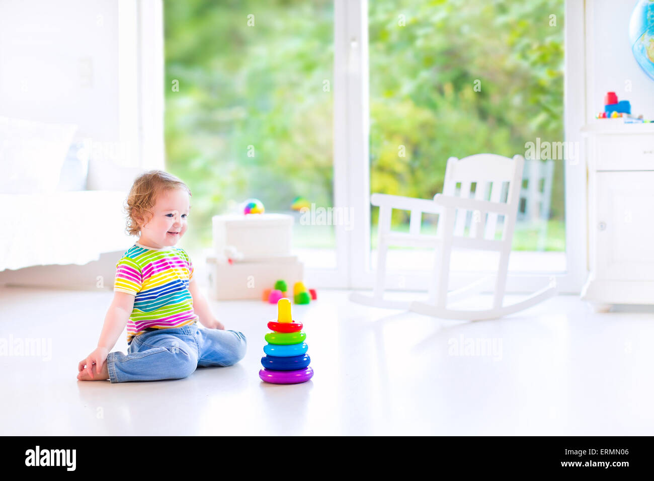 Adorable petit bébé fille dans une chemise colorée à jouer avec un jouet pyramide et blocs de construction assis sur le plancher Banque D'Images