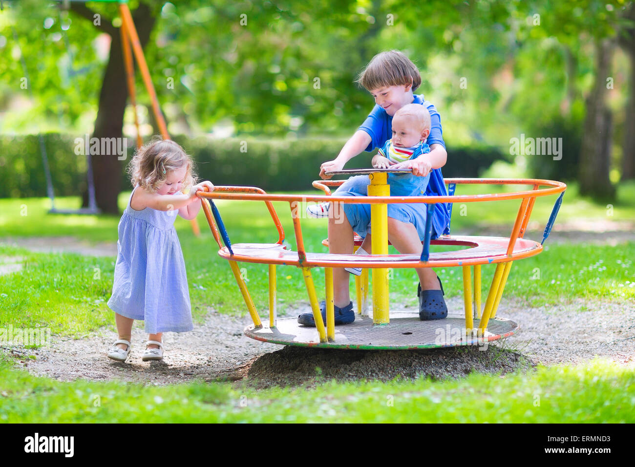 Trois des enfants heureux, rire adolescent garçon, mignon bébé et adorable bébé fille, jouer ensemble sur une aire de swing Banque D'Images