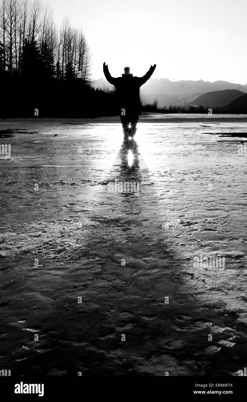 Jeune homme debout sur un lac gelé avec bras levés ; Haines, Alaska, United States of America Banque D'Images