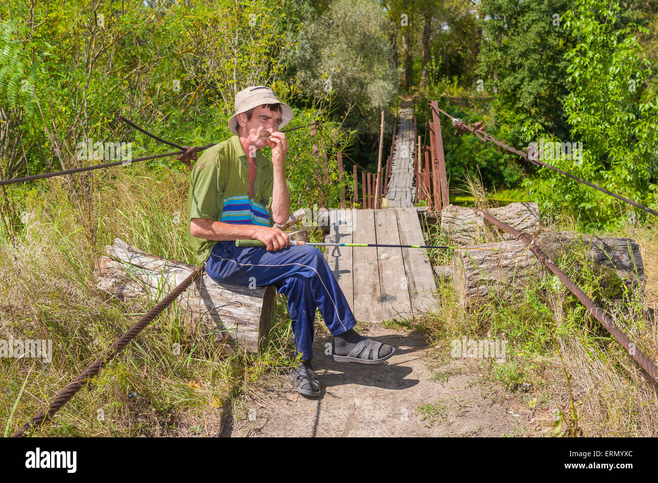 Vieux Pêcheur ukrainien assis sur un pont suspendu et cigarette roulée par lui-même Banque D'Images