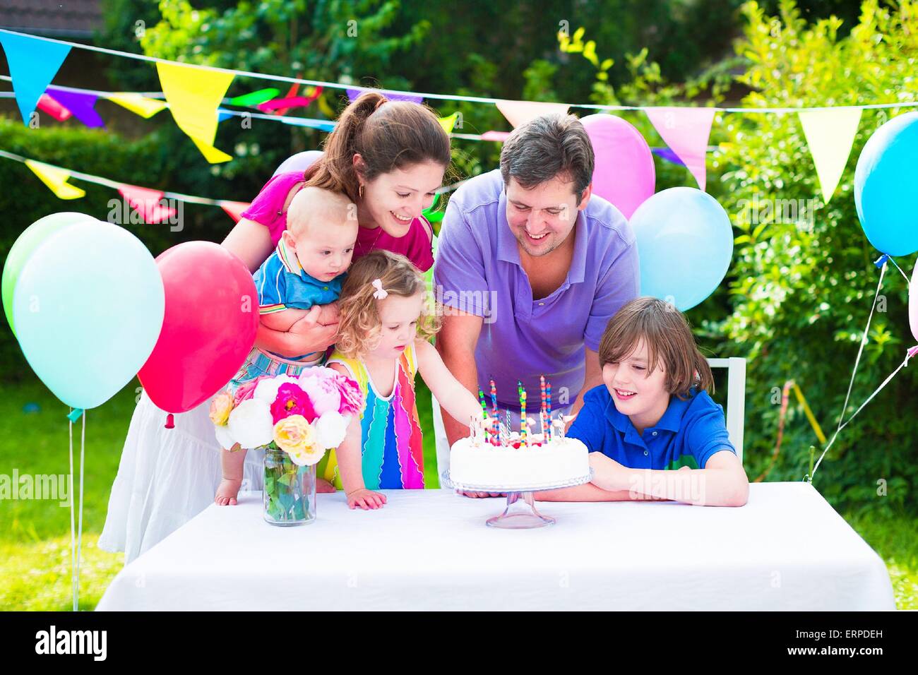 Professionnels grande famille avec trois enfants bénéficiant d'anniversaire avec gâteau blowing candles en jardin décoré avec des ballons et des bannières Banque D'Images