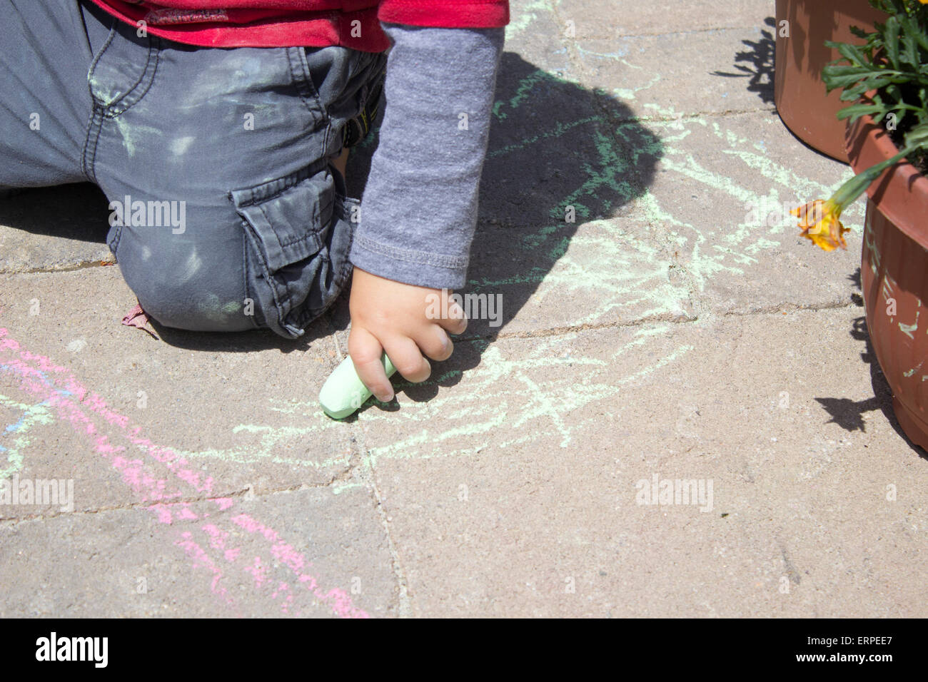 Petit Garçon jouant avec de la craie sur les pavés de ciment Banque D'Images