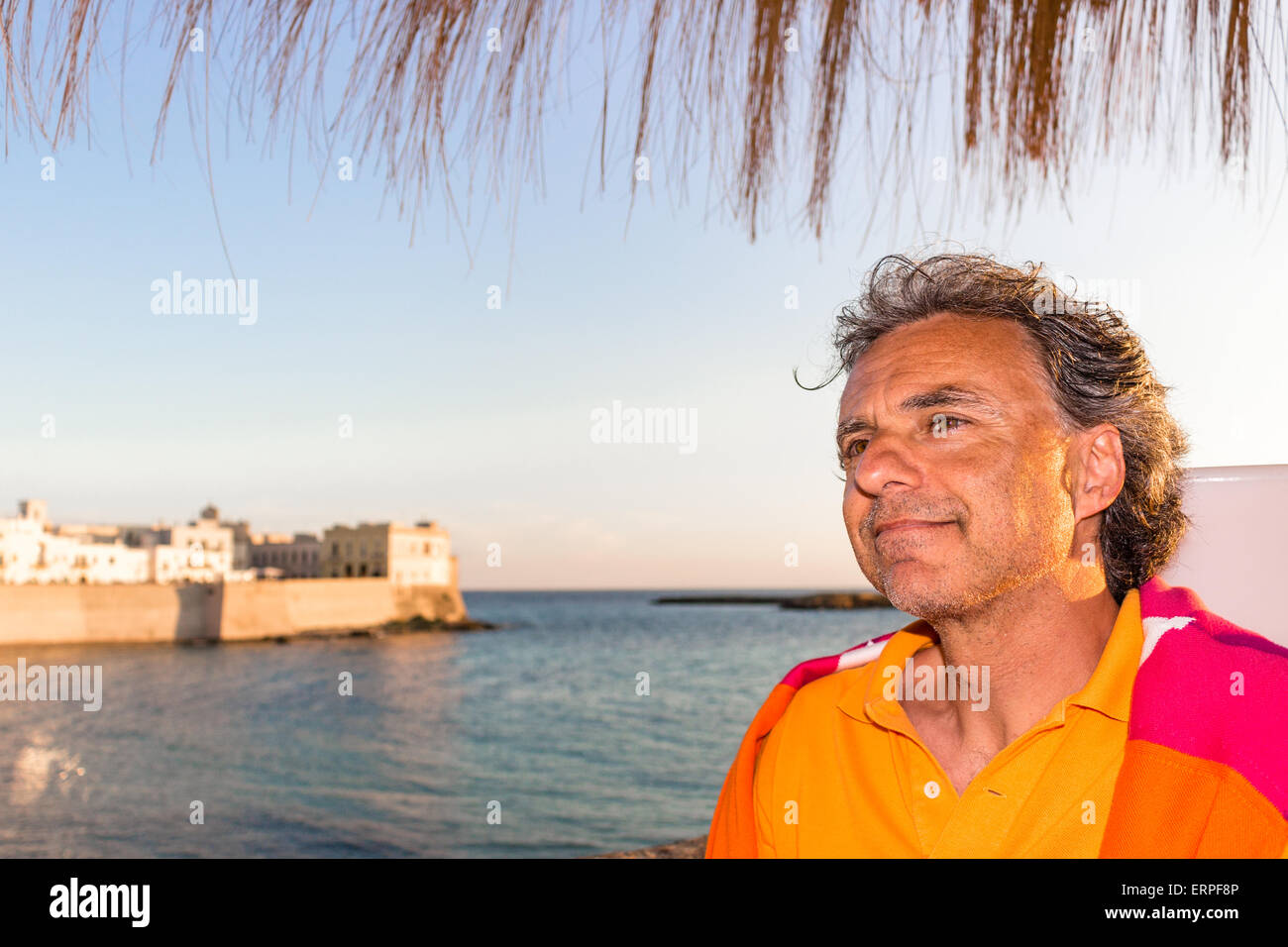 Beau bronzage homme d age moyen avec sel poivre seche dans des vetements decontractes avec pull rouge et orange et jaune polo en plein air italien il est detendue sous palm parapluie