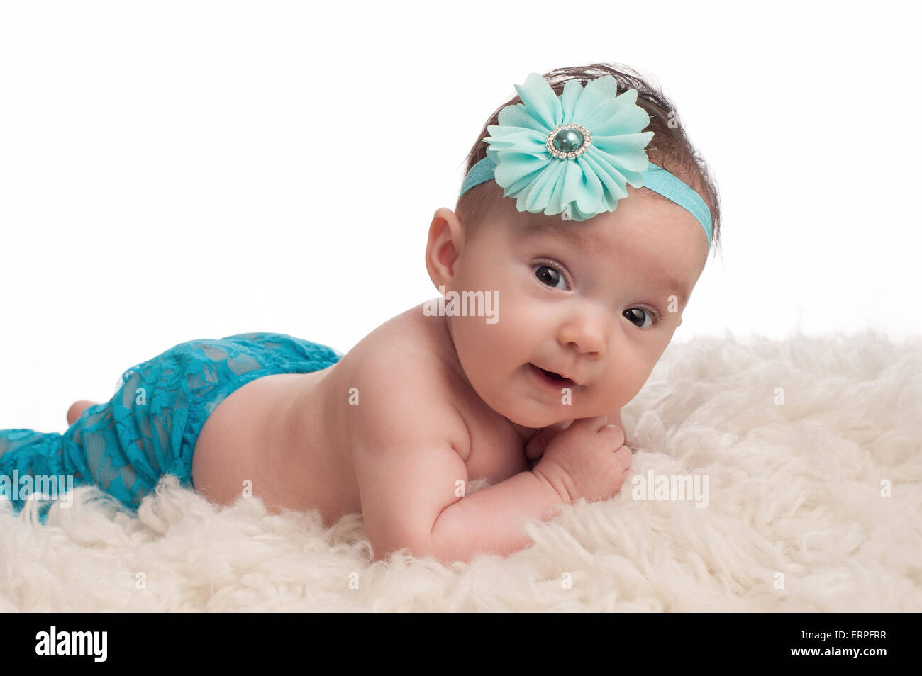 Un portrait of a happy, 3 mois bébé fille portant un bandeau de fleurs bleu turquoise. Elle est couchée sur le ventre, appuyée au Banque D'Images