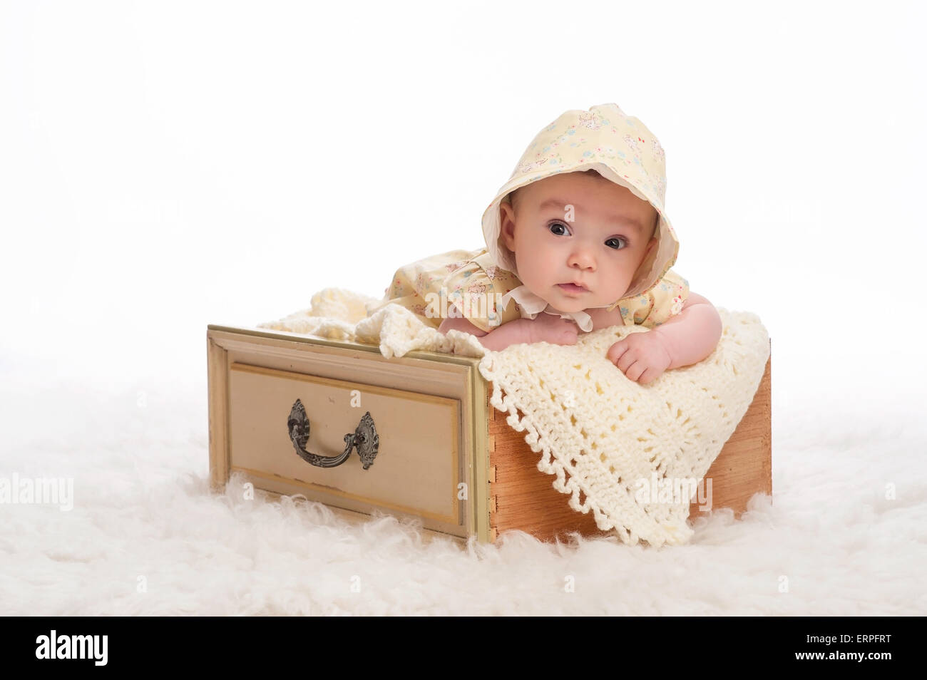 Un bébé de trois mois fille portant un bonnet jaune et couché dans un tiroir jaune vintage. Banque D'Images