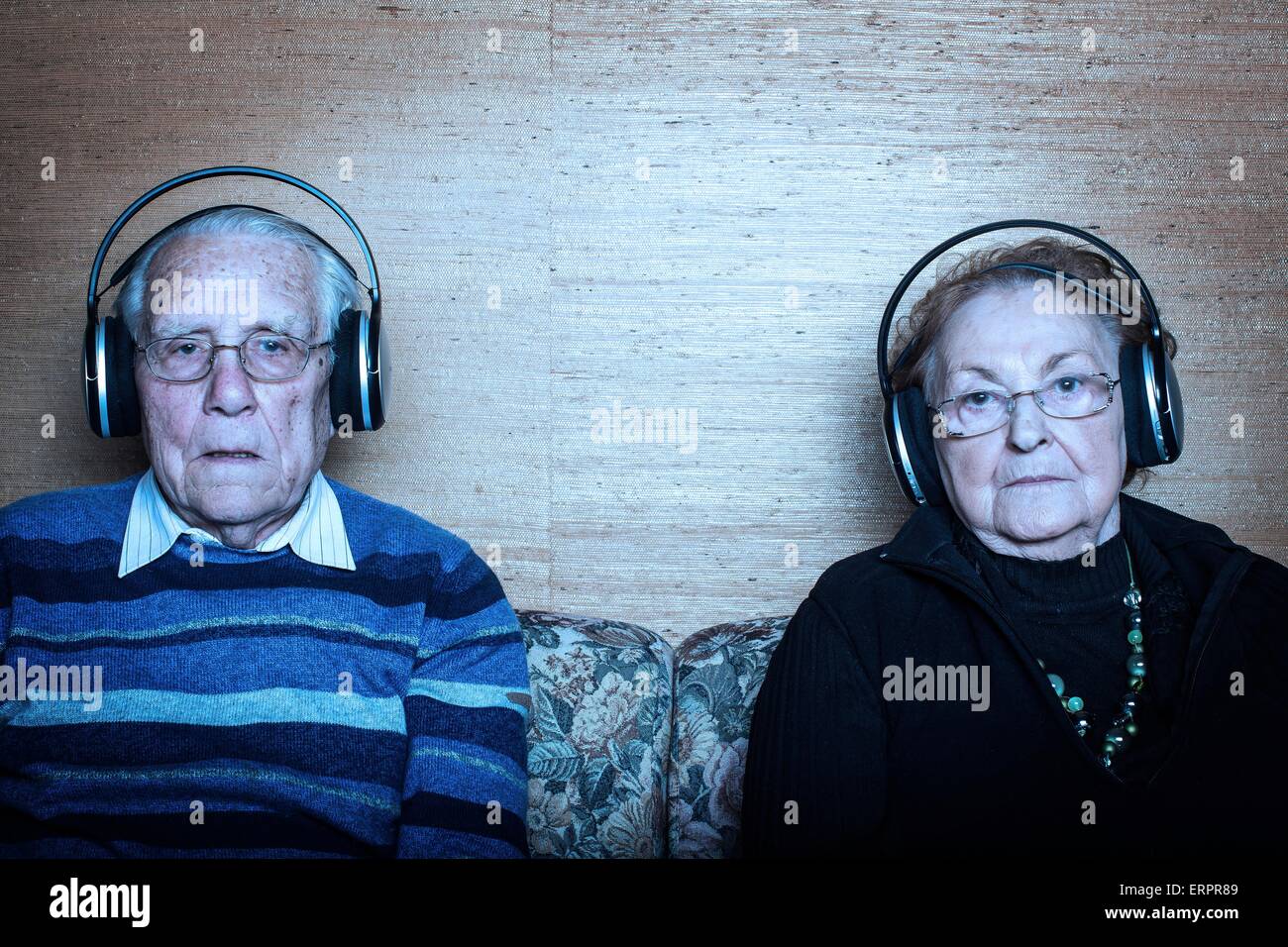 Parution du modèle. Senior couple sitting on sofa portant des écouteurs. Banque D'Images