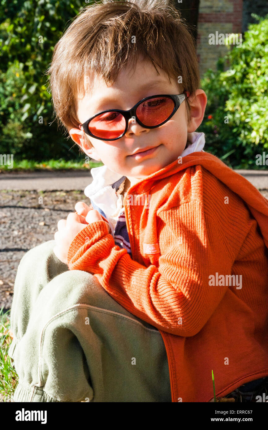 Enfant caucasien, garçon de 3-4 ans, assis à l'extérieur avec dos contre  l'arbre et portant des lunettes de soleil. Visage tourné vers le  spectateur. Contact visuel, sourire Photo Stock - Alamy