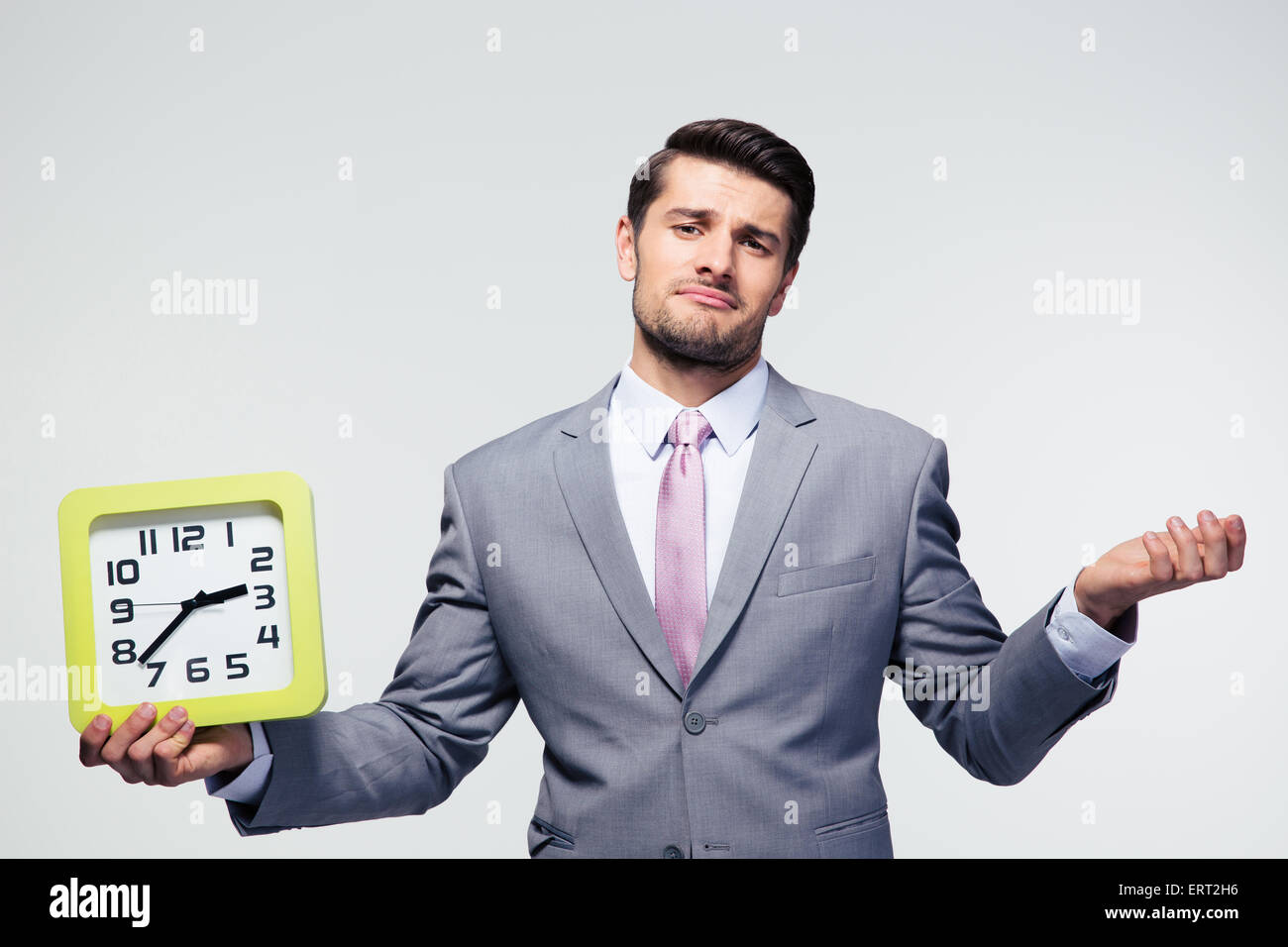 Businessman holding clock et copyspace sur fond gris. Looking at camera Banque D'Images