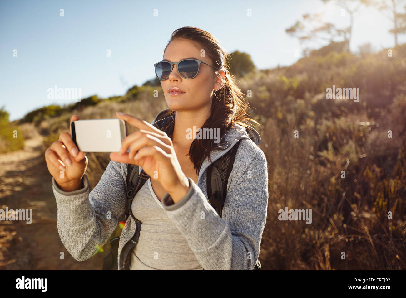 Jeune femme randonneuse prenant des photos avec son téléphone portable. Caucasian woman photographing landscape with smartphone. Banque D'Images