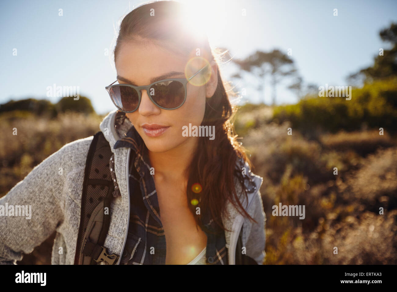 De plein air randonnée dans une réserve naturelle au soleil. Pretty young female hiker portant des lunettes de soleil à la recherche vers le bas avec su Banque D'Images