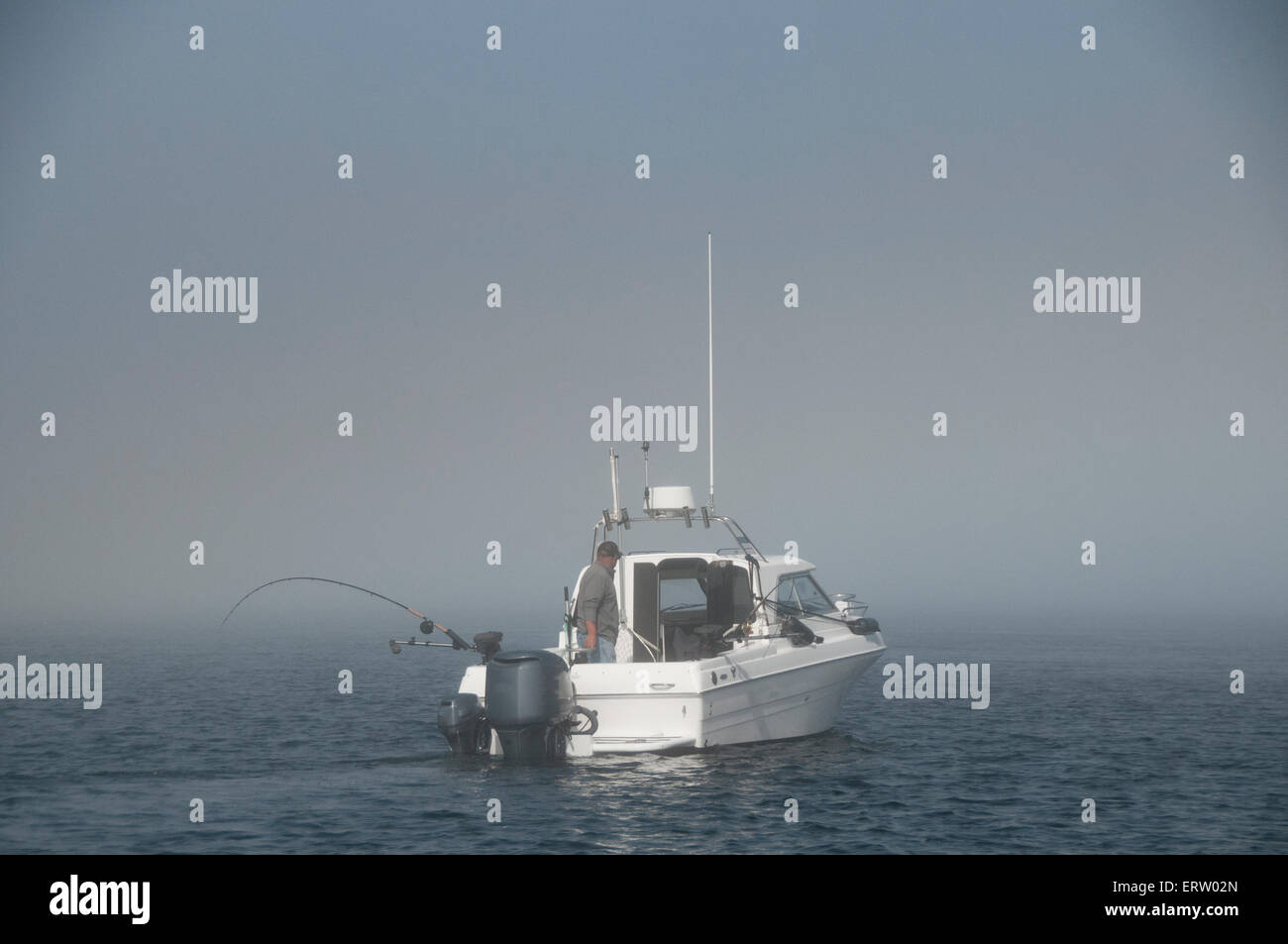 Pêcheur sportif en solo dans un bateau sur la côte ouest du Canada à la traîne du saumon avec de l'eau calme, ciel bleu et léger brouillard marin Banque D'Images