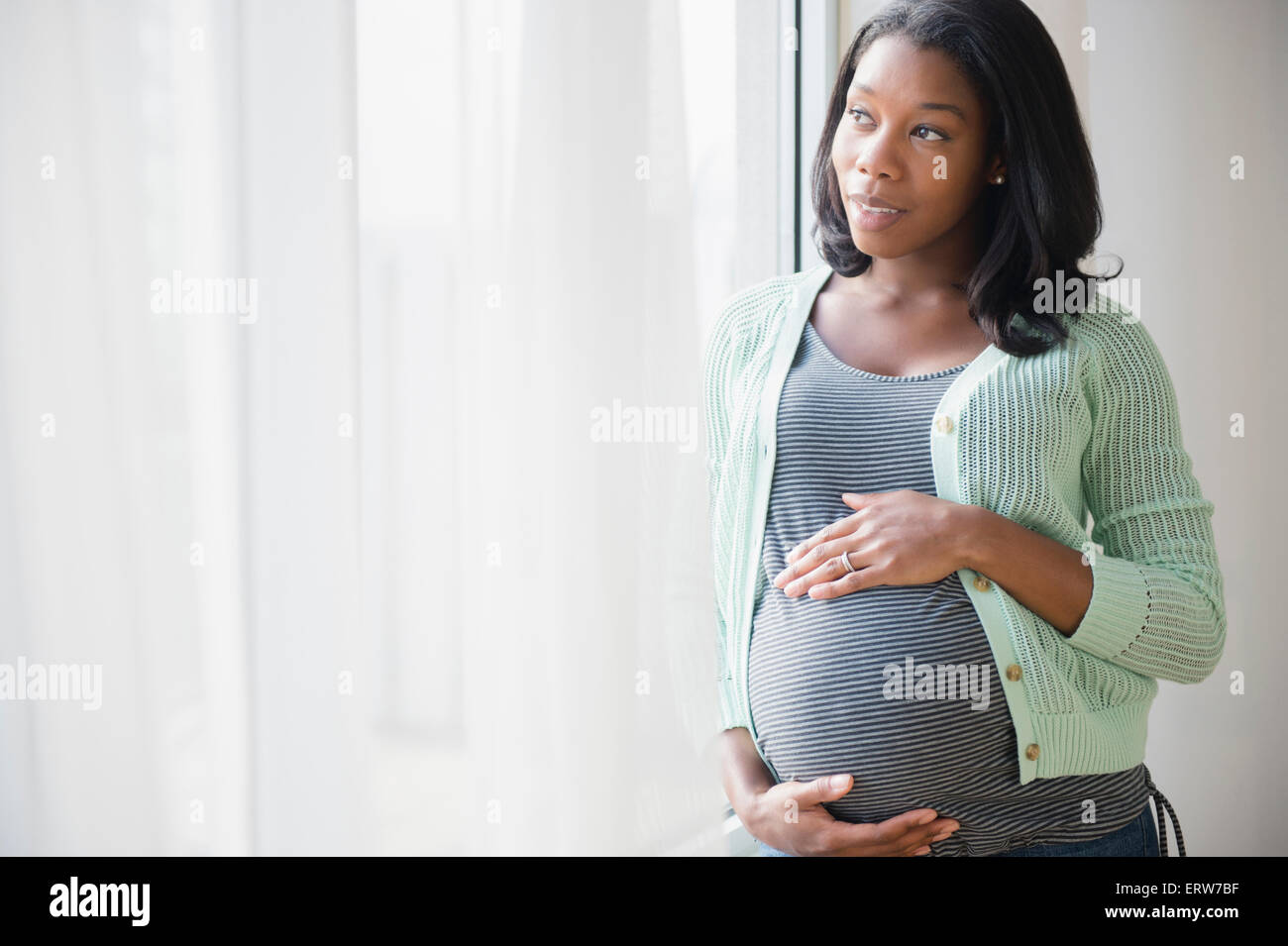 Black pregnant woman holding son estomac at window Banque D'Images