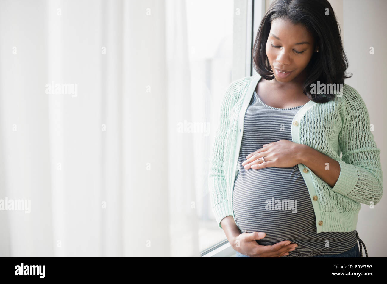 Black pregnant woman holding son estomac at window Banque D'Images