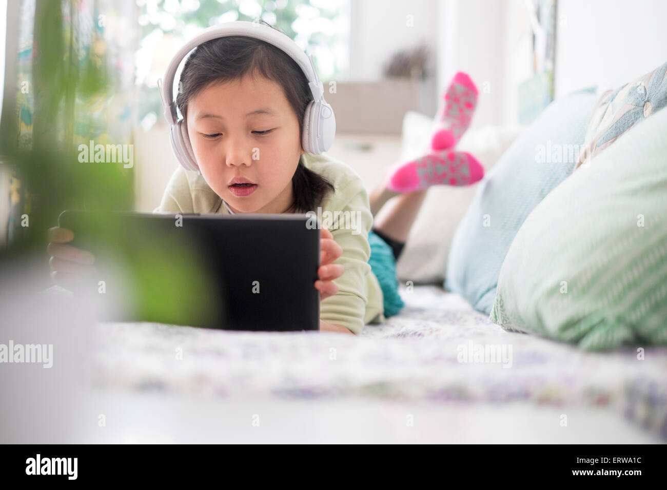 Chinese girl using digital tablet with headphones on bed Banque D'Images