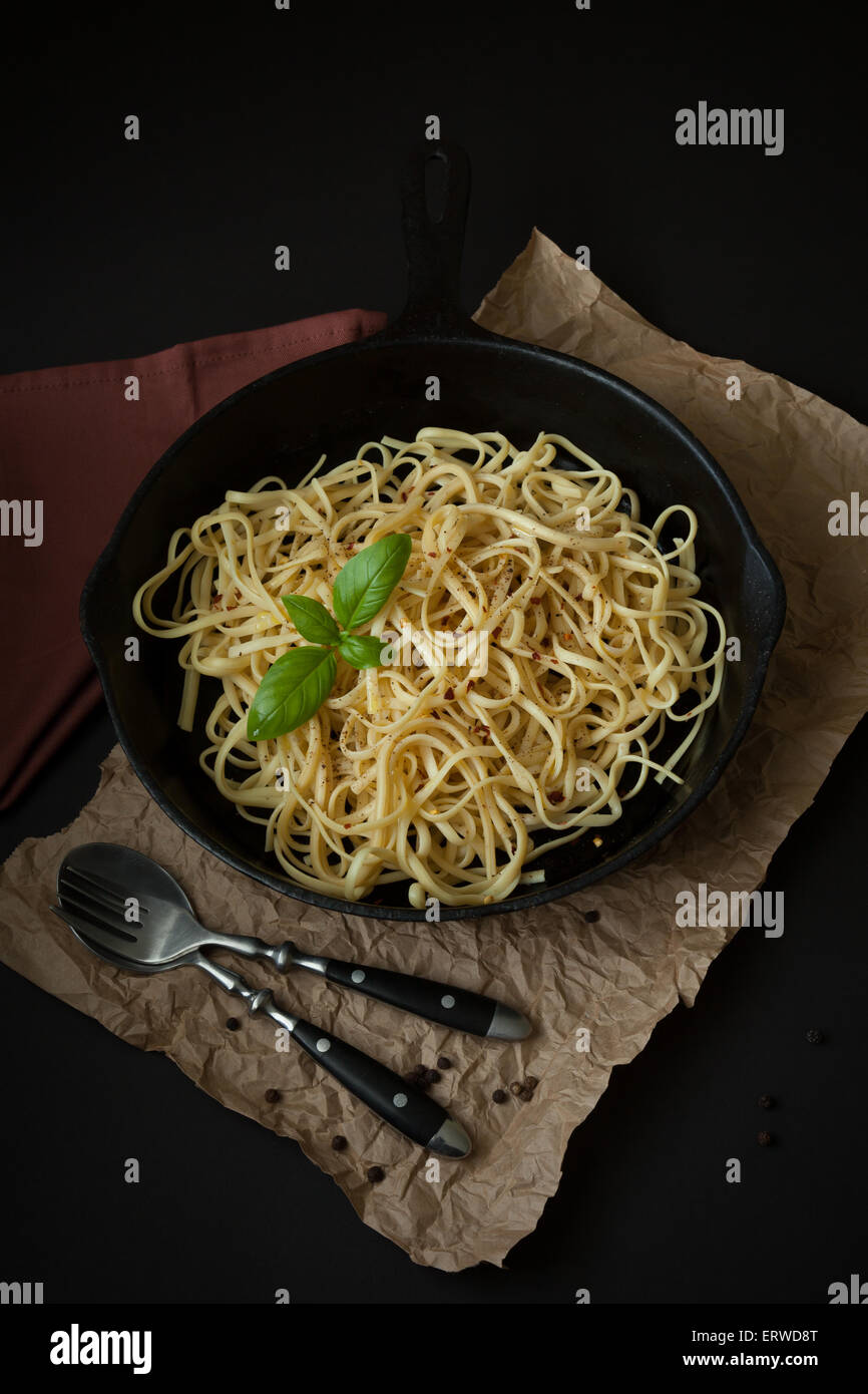 L'intérieur d'un siège Linguine poêle en fonte noire sur une surface noire avec un sac en papier brun froissé en dessous. Banque D'Images