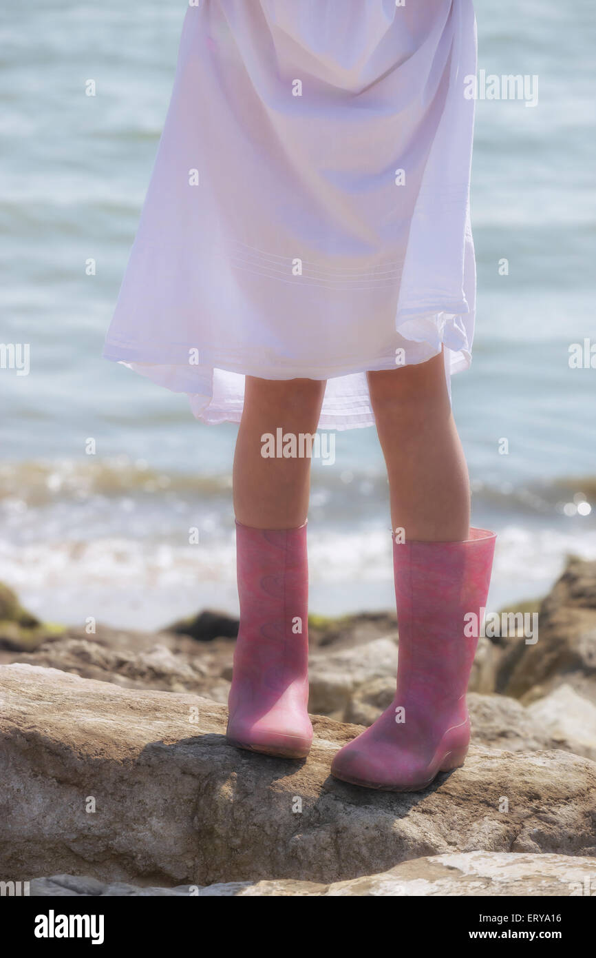 Les jambes d'une fille avec Wellies sur rochers à la mer Banque D'Images