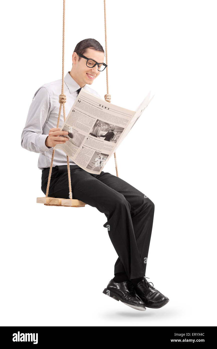Shot vertical d'un jeune homme gai lire un journal assis sur une balançoire isolé sur fond blanc Banque D'Images