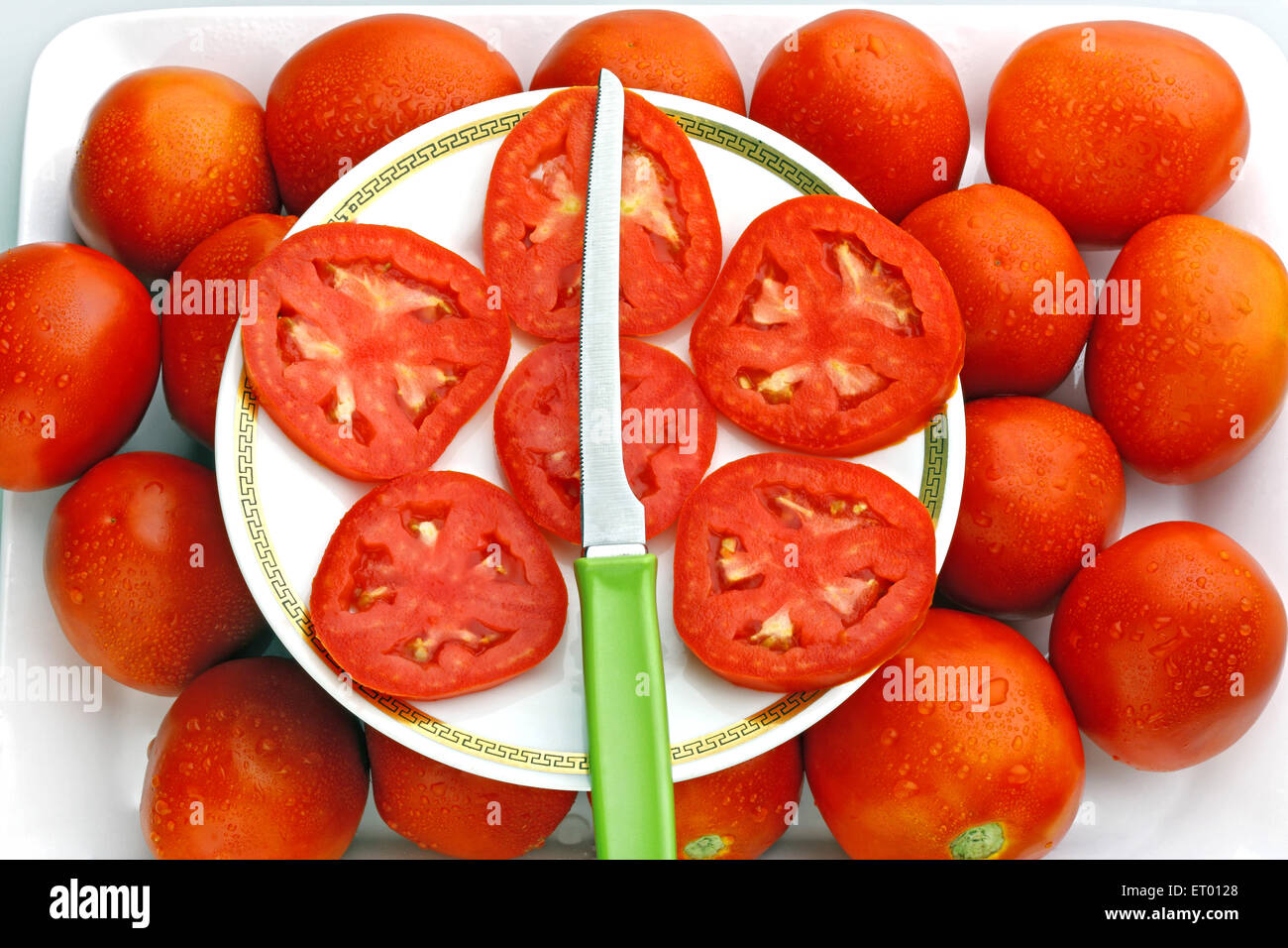Les tomates rouges Amérique Lycopersicon esculentum tranches sur une plaque blanche avec un couteau ; Inde Banque D'Images