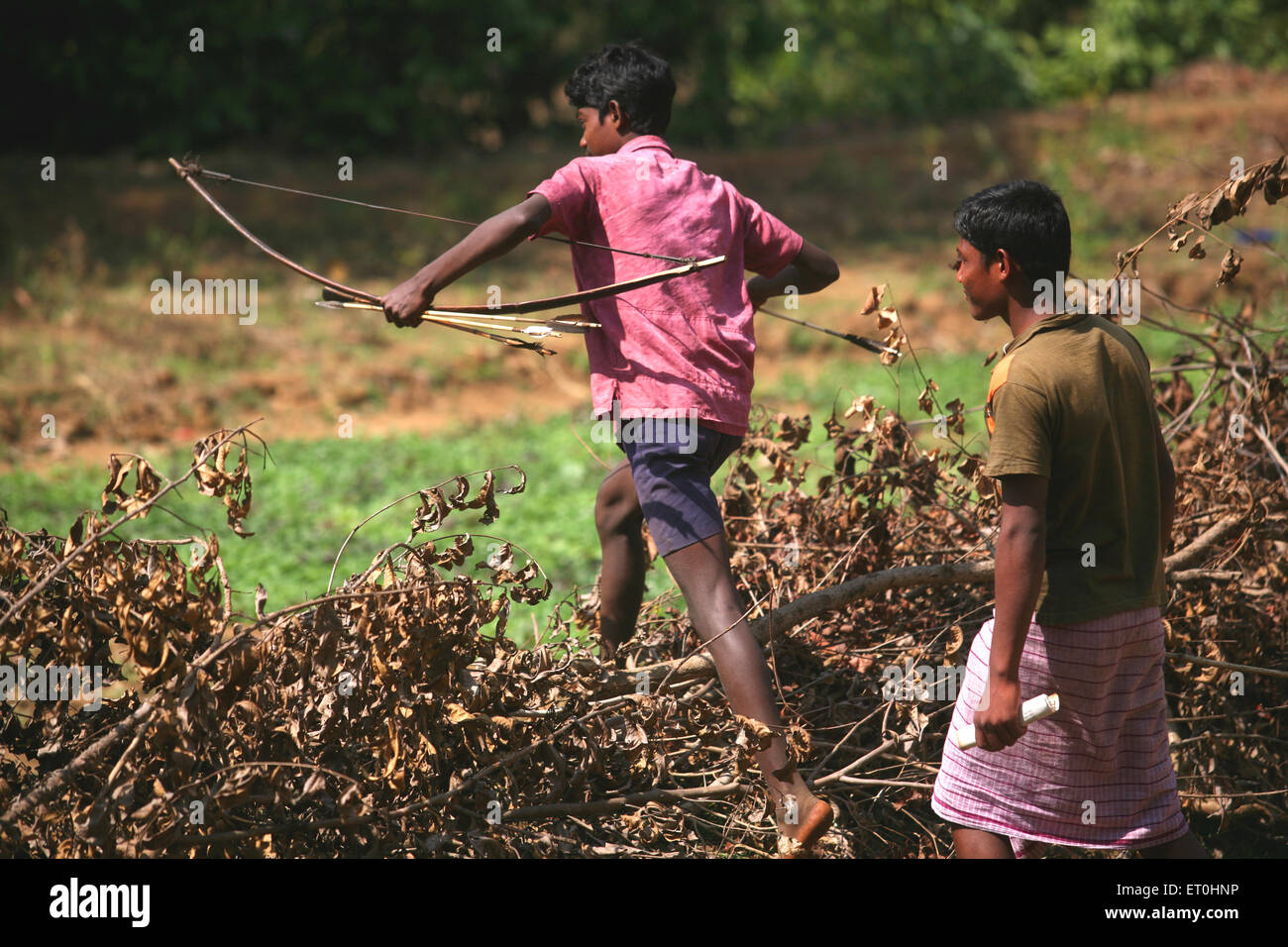 Jeune garçon tribal avec arc et flèche marcher sur les forêts sèches avec ami ; Jharkhand en Inde ; Banque D'Images