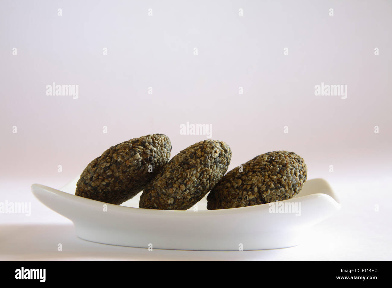 Doux indien, Tilgur ladoo, tilgul ladoo, graines de sésame noir ladoo, dans une assiette sur fond blanc Banque D'Images