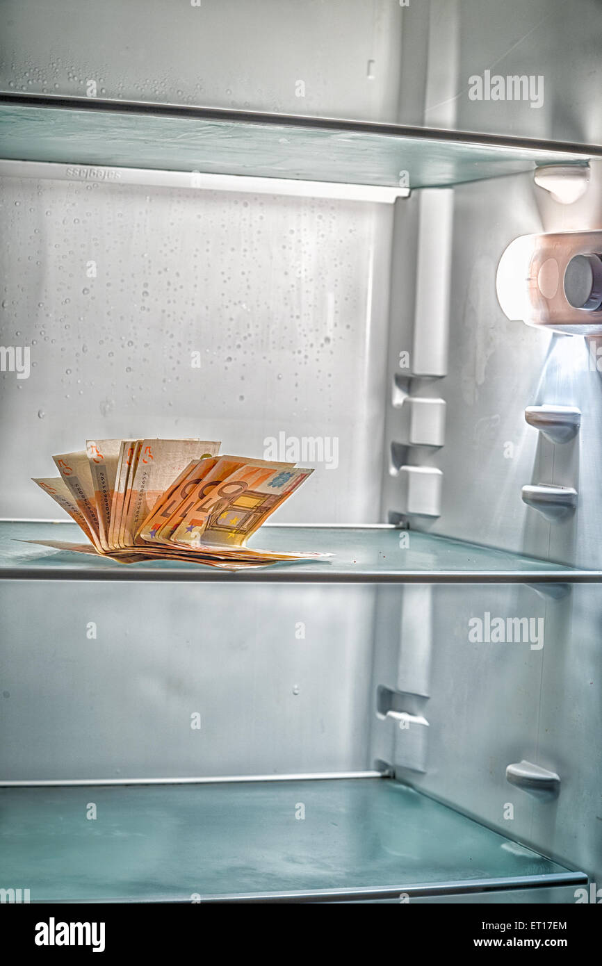 De l'argent frais dans le réfrigérateur : une poignée de billets de 50 euros éclairé par la lumière froide d'un réfrigérateur vide Banque D'Images