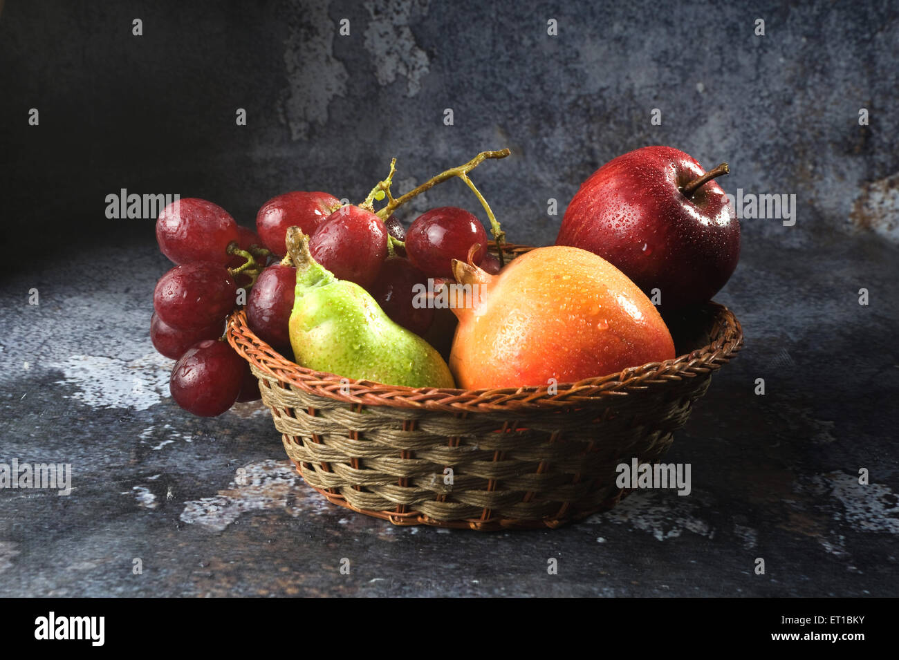 Les gouttes d'eau ; des fruits sur la grenade ; apple ; poire et raisin dans le panier en bois en arrière-plan Banque D'Images
