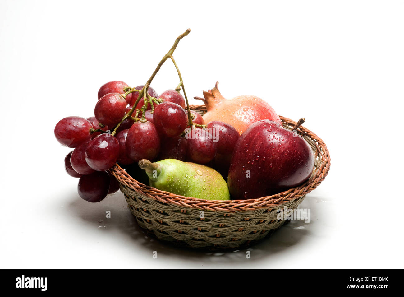 Les gouttes d'eau ; des fruits sur la grenade ; apple ; poire et raisin dans le panier en bois sur fond blanc Banque D'Images