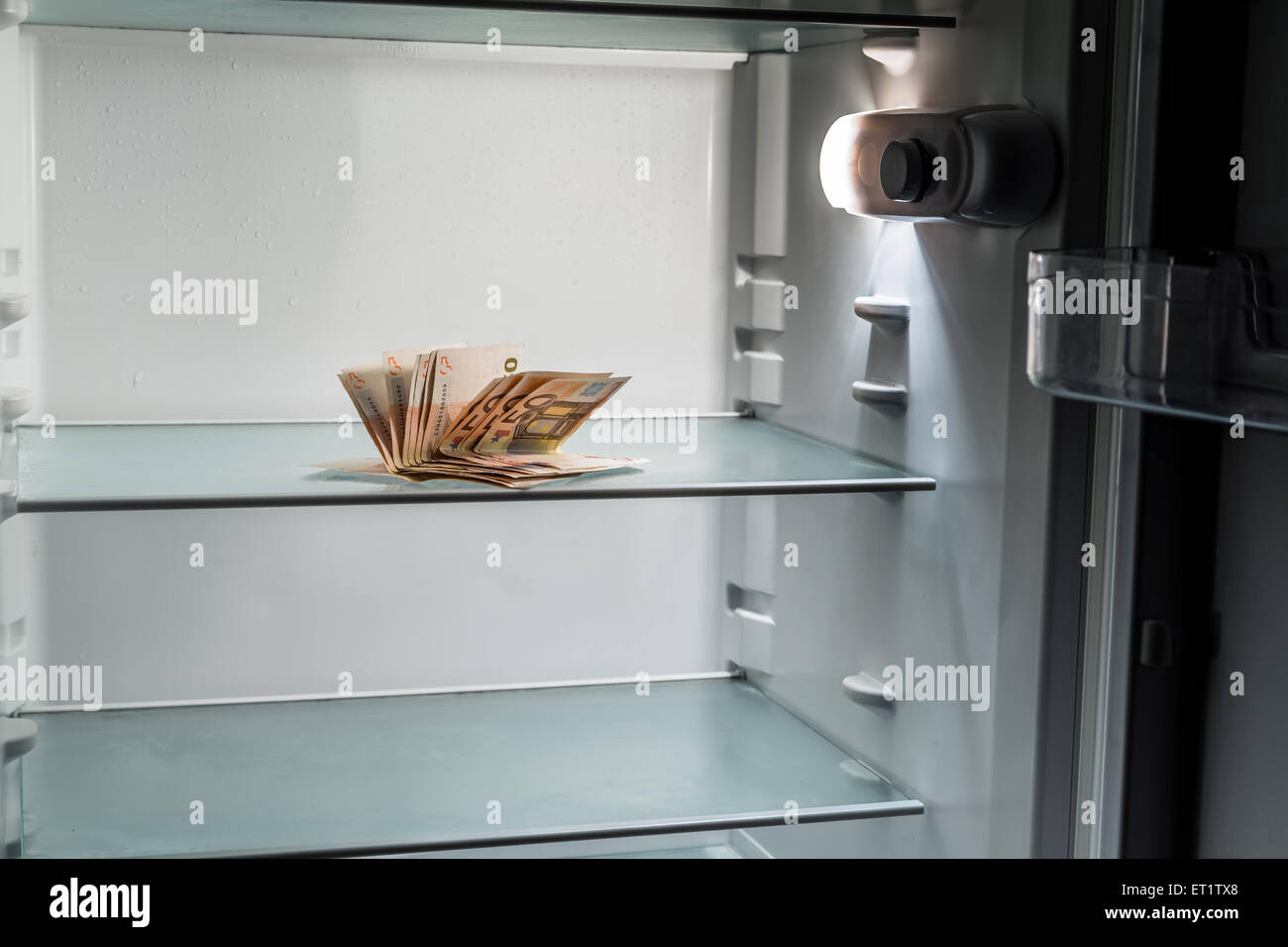 De l'argent frais dans le réfrigérateur : une poignée de billets de 50 euros éclairé par la lumière froide d'un réfrigérateur vide Banque D'Images