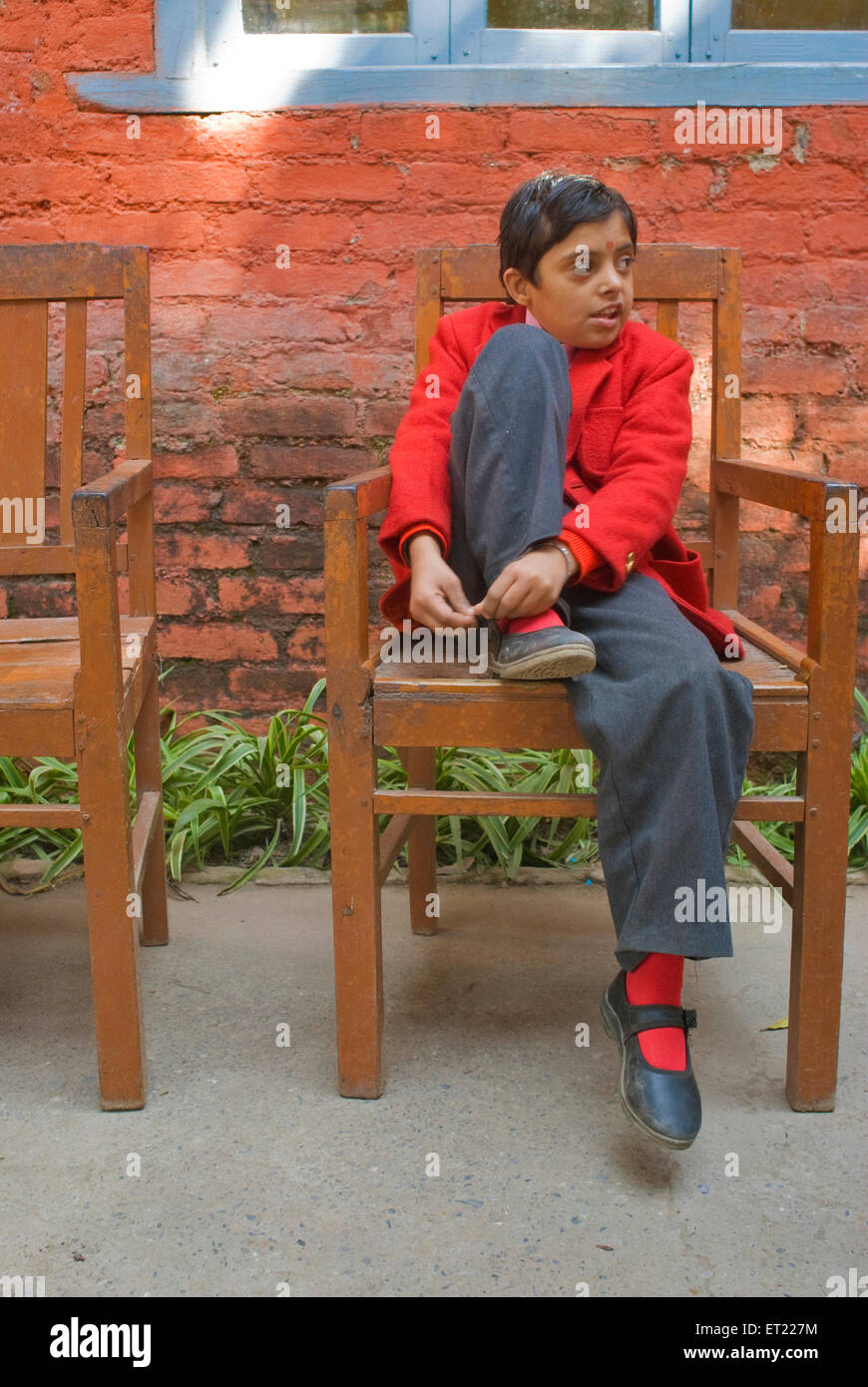 Lier sa fille chaussures noires assis sur une chaise en manteau rouge ; Nanhi Duniya ; école ; Uttarakhand Uttaranchal Dehra Dun Banque D'Images