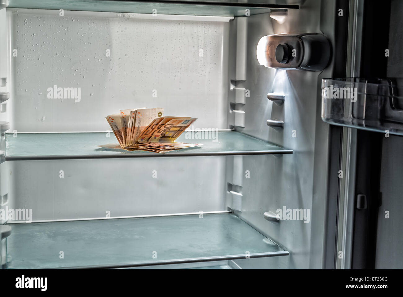 De l'argent frais dans le réfrigérateur : une poignée de billets de 50 euros éclairé par la lumière froide d'un réfrigérateur vide Banque D'Images