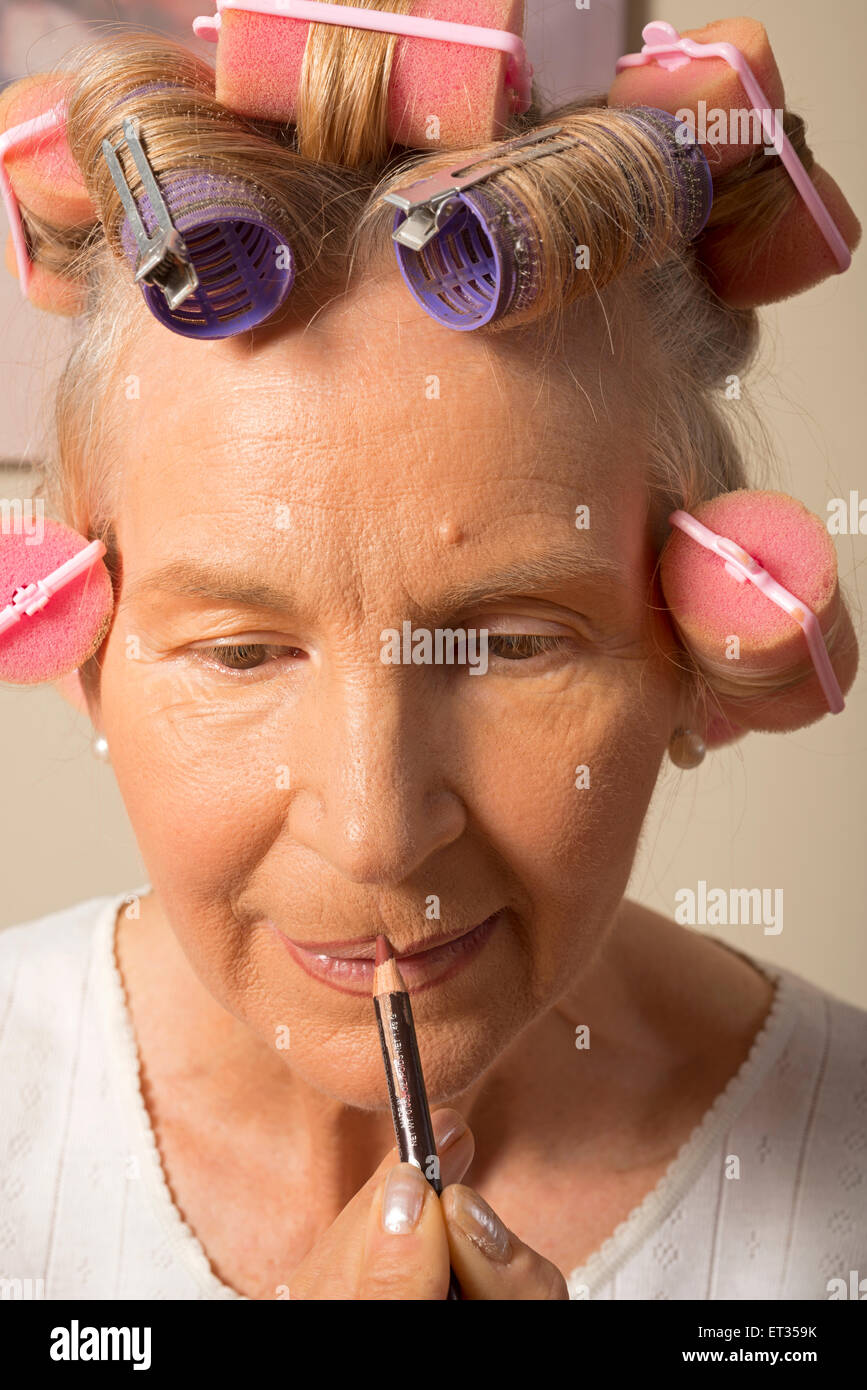 Woman in curlers appliquant un brillant à lèvres au crayon Banque D'Images