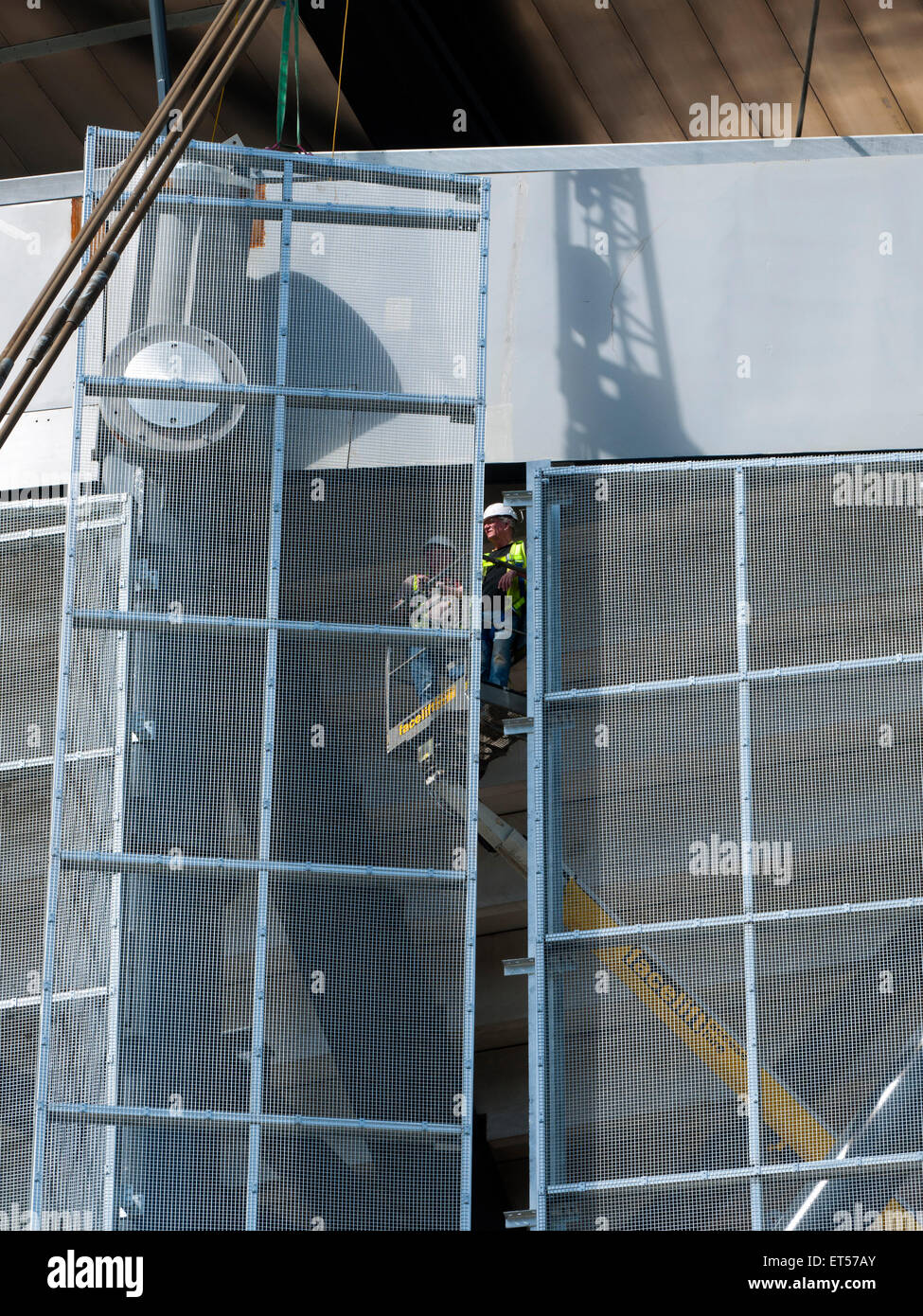 Des ouvriers sur une plate-forme d'accès de l'installation des panneaux à mailles, tribune sud travaux d'agrandissement, l'Etihad Stadium, Manchester, Angleterre, RU Banque D'Images