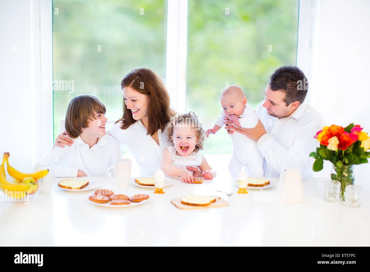 Heureux jeune famille avec enfants arbre s'amusant un dimanche matin, le petit-déjeuner dans une salle blanche avec une grande fenêtre Banque D'Images