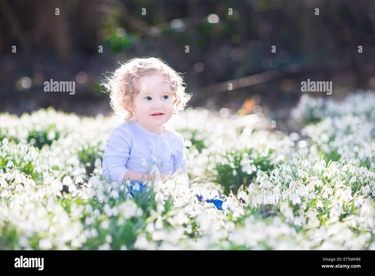 Belle curly bébé fille jouant avec les premières fleurs du printemps dans un magnifique parc ensoleillé de printemps Banque D'Images