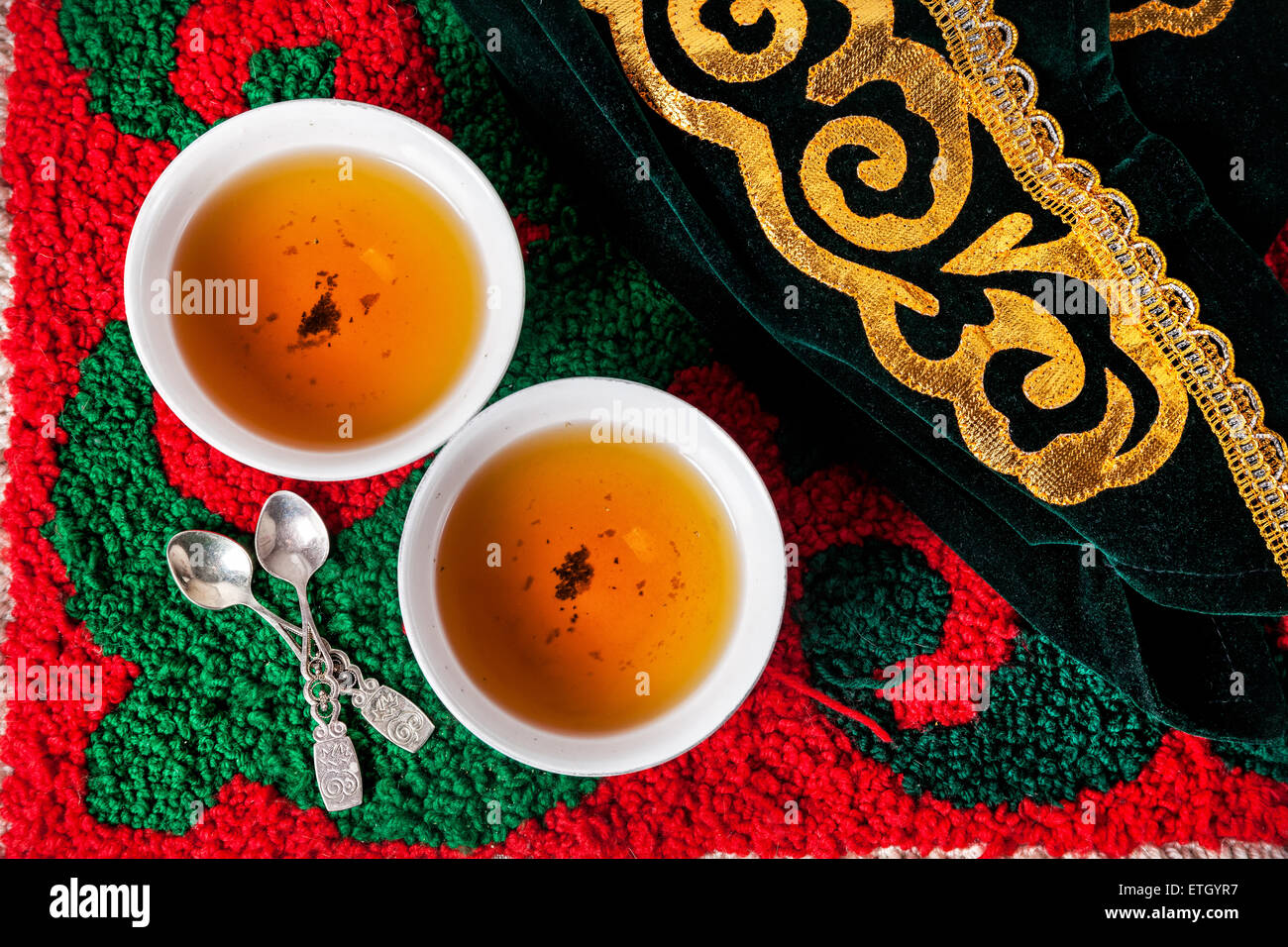 Hat nationale kazakhe et thé noir en deux teabowls sur les tapis rouge avec motif vert oriental Banque D'Images