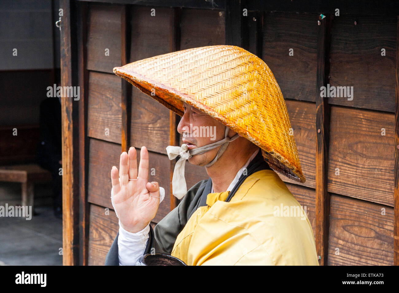 Kyoto. Gros plan, tête et épaule de prêtre bouddhiste, moine, debout dans la rue avec la main levée à bénir, porte un chapeau de bambou, robe jaune Banque D'Images