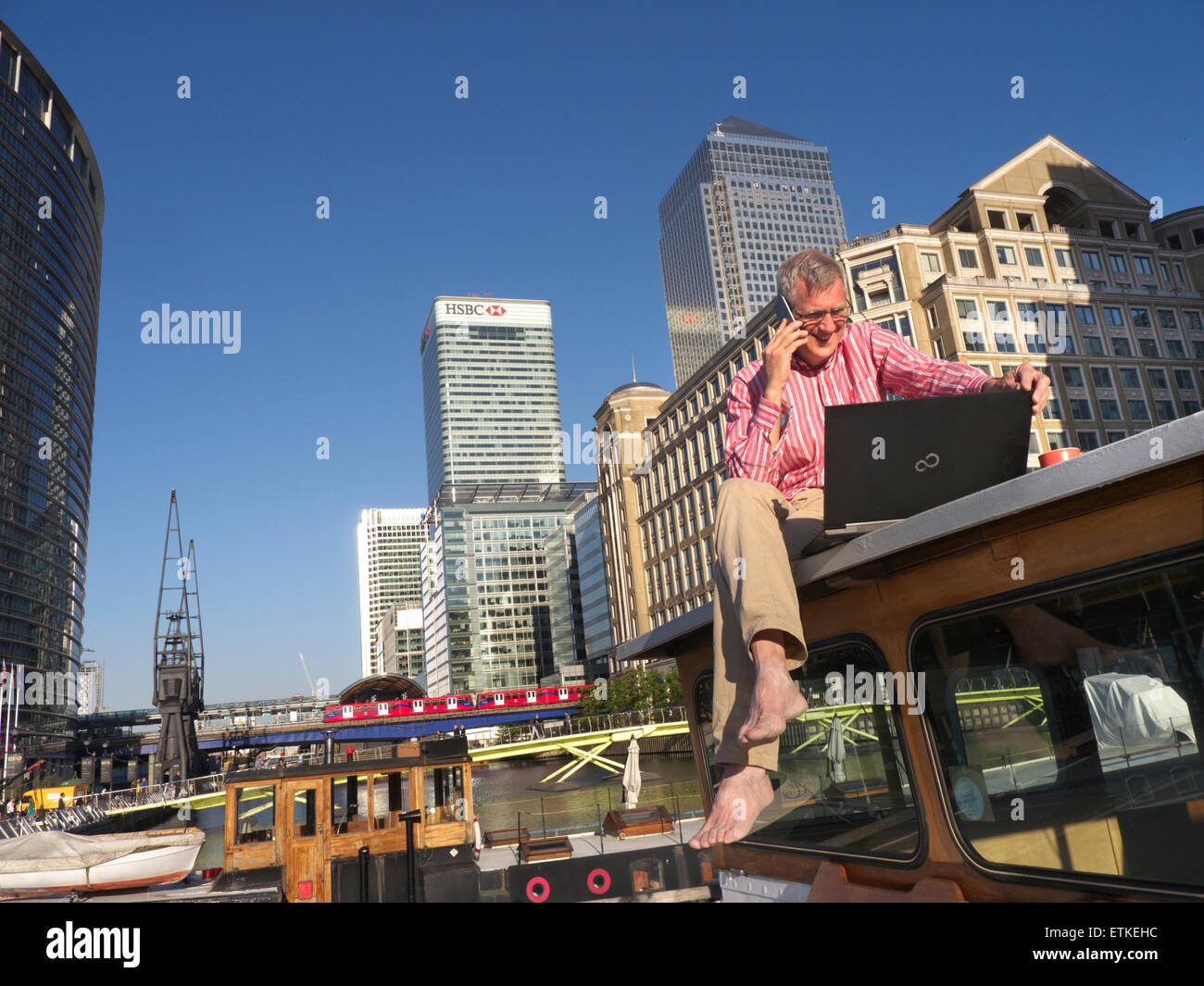 Man dehors sur son bateau de parler sur l'iPhone 6 à son ordinateur portable à Canary Wharf bureaux situés derrière Londres E14 Banque D'Images