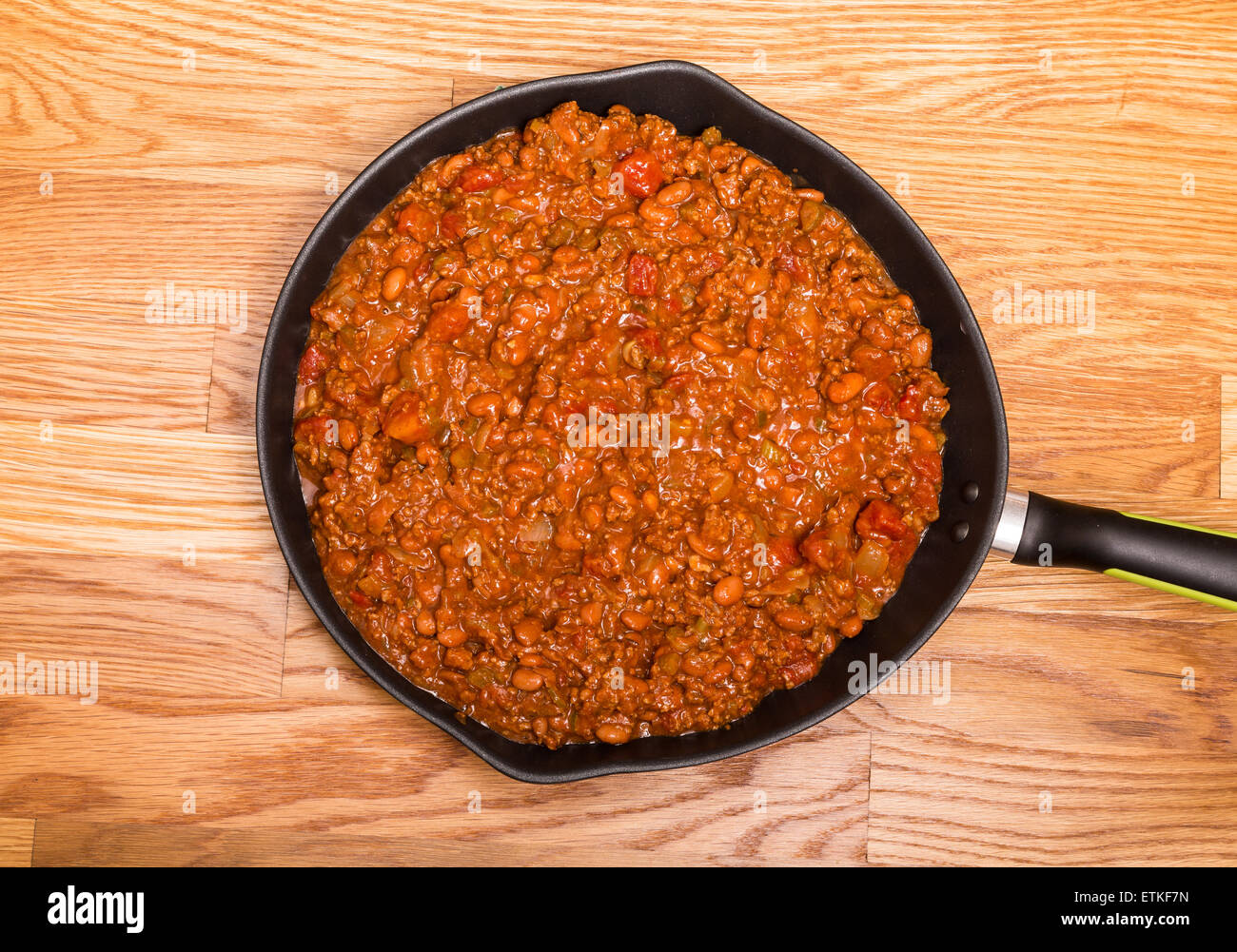 Chili avec de la viande et les haricots dans une poêle de fer noir sur une table en bois Banque D'Images