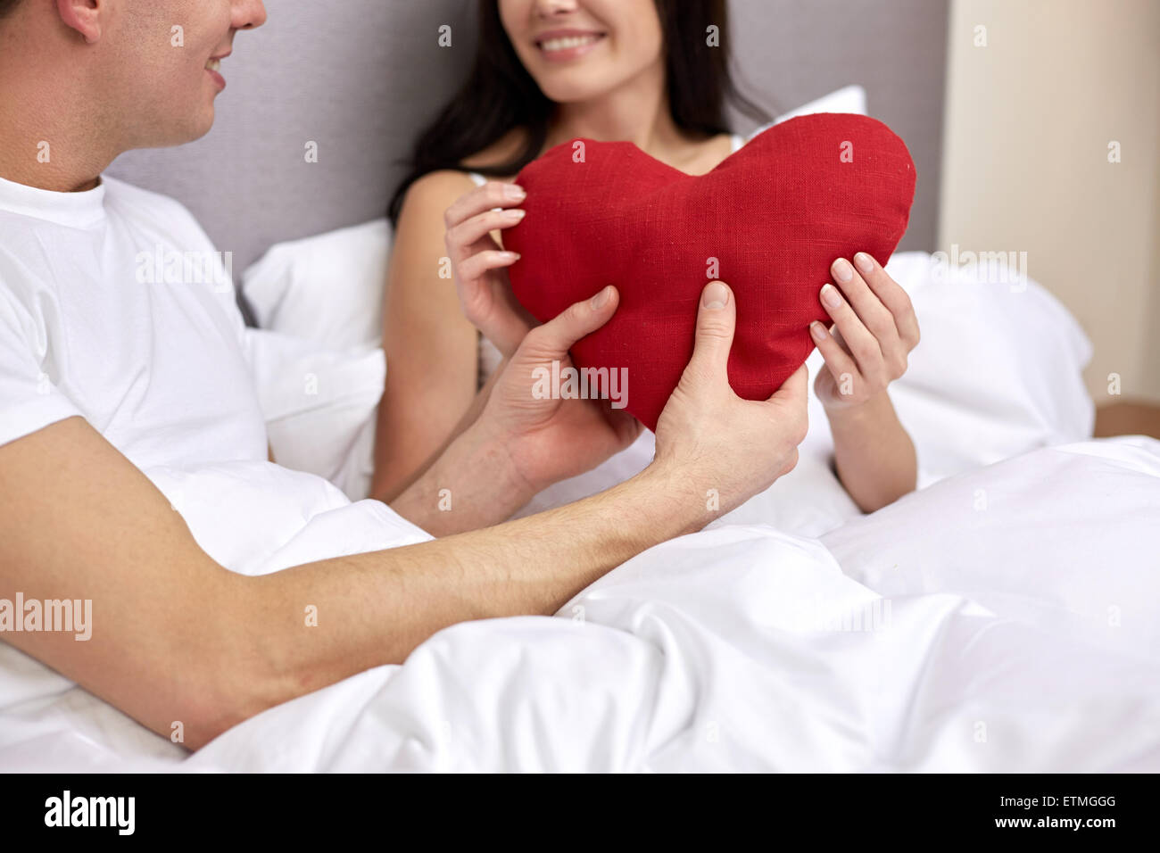 Smiling couple au lit avec oreiller en forme de coeur rouge Banque D'Images