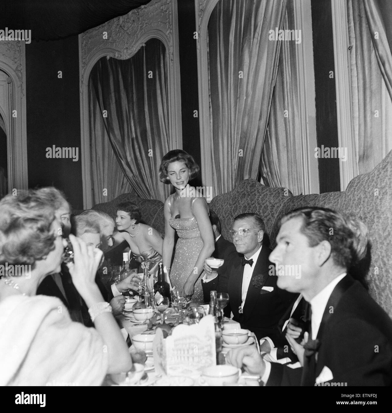 Parmi les invités à une fête organisée par Laurence Olivier et Lauren Bacall. Lauren Bacall sur le point de s'asseoir, avec des invités déjà à la table, y compris, Laurence Olivier et Kenneth plus. 10 novembre 1958. Banque D'Images