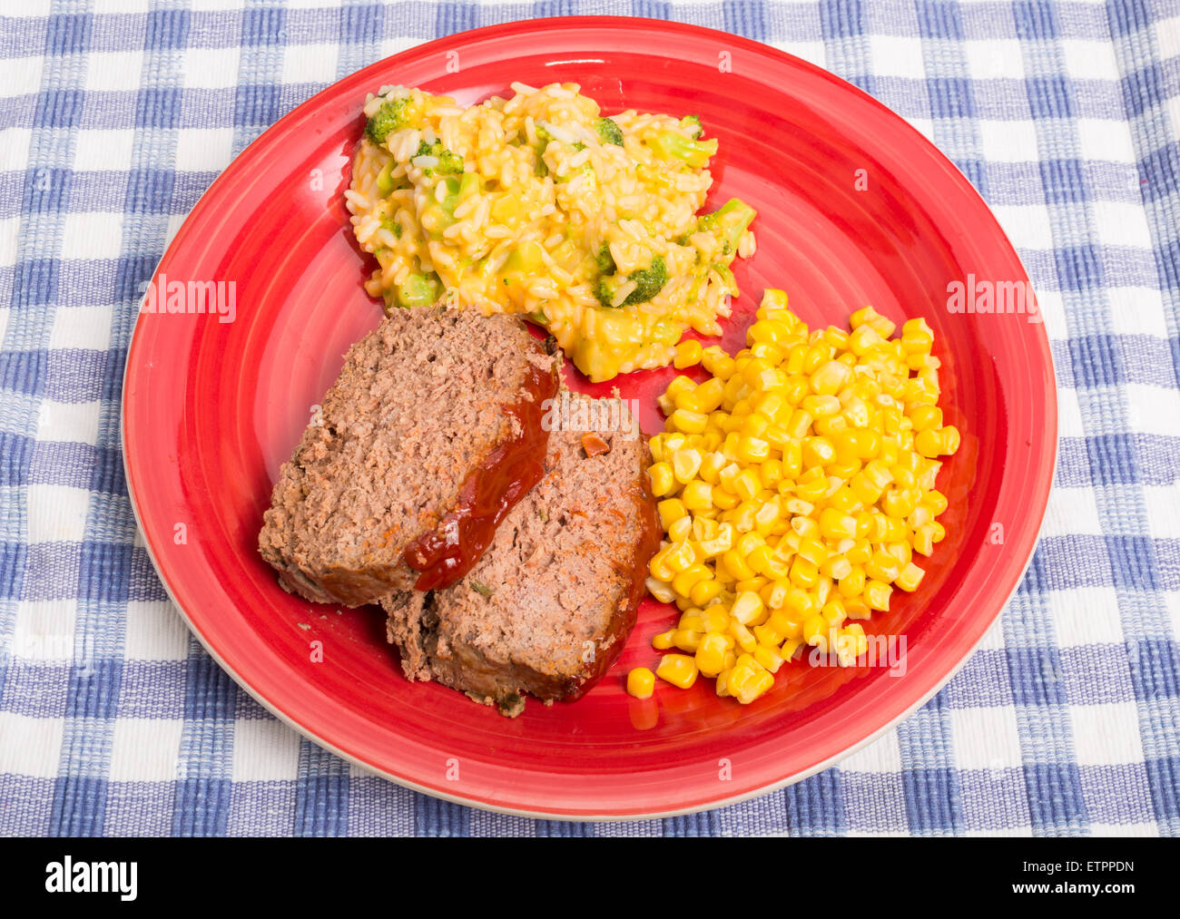 Tranches de viande, de maïs et de riz brocoli au fromage sur une plaque rouge sur un tapis à carreaux bleu Banque D'Images
