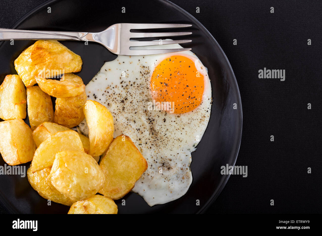 Un œuf frit sur la plaque noire avec des pommes et de la fourchette - angle ci-dessus Banque D'Images