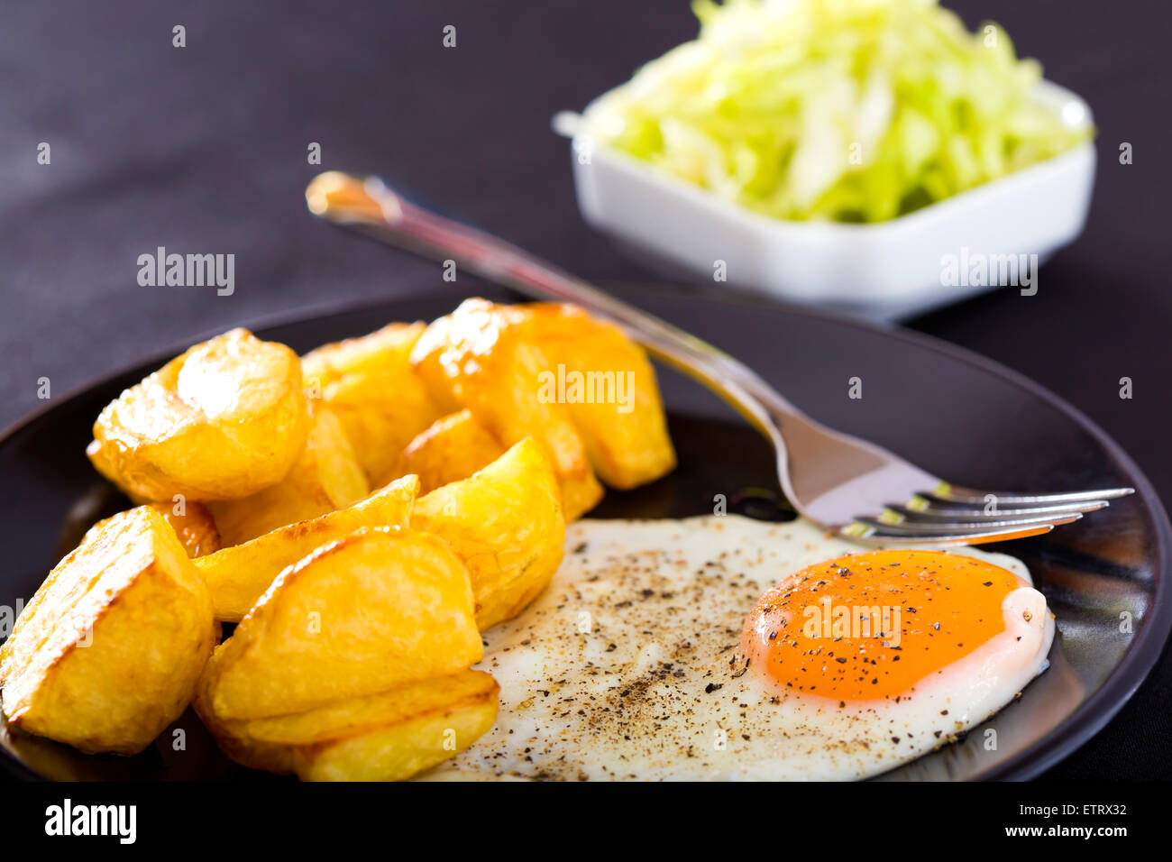 Près d'un œuf frit sur la plaque noire avec des pommes de terre et la fourche Banque D'Images