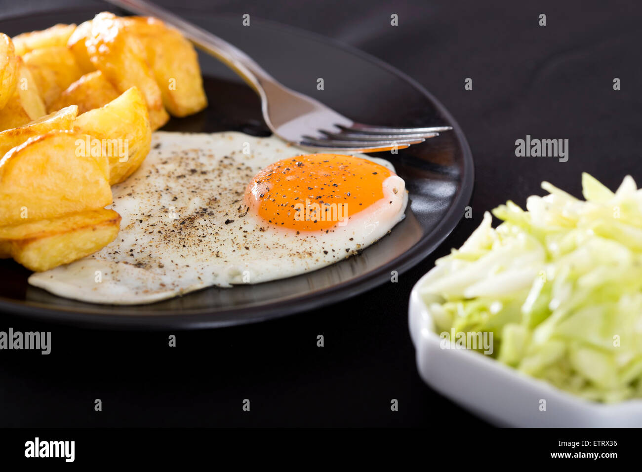 Près d'un œuf frit sur la plaque noire avec des pommes de terre et la fourche Banque D'Images