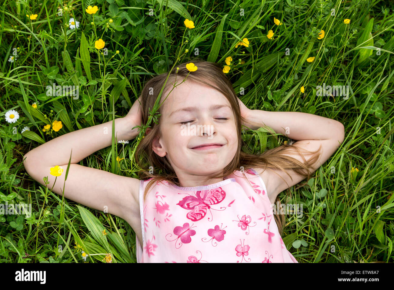 Portrait of smiling little Girl with closed eyes lying on a flower meadow Banque D'Images